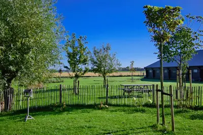 a fence with a picnic table and trees in a field at Het Gouwe Boetje in Hoogwoud