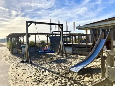two children playing on a swing set on the beach at Cosy beach house for ocean & nature lovers in Noordwijk