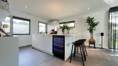 a kitchen with white cabinets and a bar with a stool at VILLA ARYVE in See-, Strand- und Golfplatznähe inklusive NETFLIX, Bad en Suite und Wohlfühlgarantie in Dirkshorn