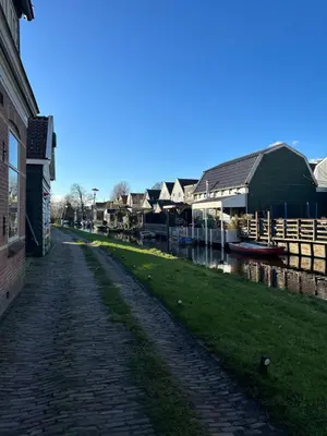 a cobblestone street next to a canal with houses at Het Kraaienest in Zaandam