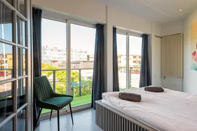 a bedroom with a bed and a chair and windows at Wind - Modern beach house in Bergen aan Zee