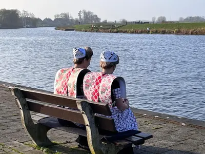 two people sitting on a bench by the water at B&B 'Op Eemdijk' in Eemdijk