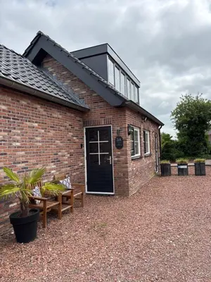 a brick house with a black door and two benches at B&B 'Op Eemdijk' in Eemdijk