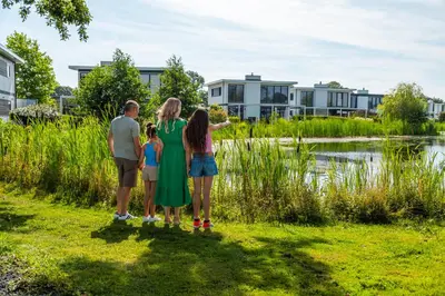 a family standing in the grass near a lake at Comfort Rooms by EuroParcs Bad Hulckesteijn in Nijkerk
