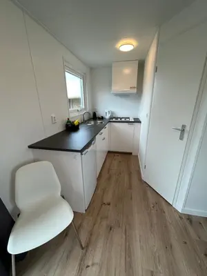 a white kitchen with a white chair and a counter at Tiny House in de duinen van IJmuiden aan Zee in IJmuiden
