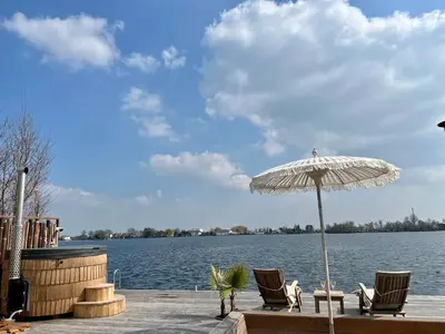 a patio with chairs and an umbrella next to the water at NEW - LITTLE IBIZA, on a lake near Amsterdam, with HOT TUB! in Vinkeveen