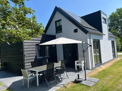 a table and chairs with an umbrella in front of a house at Villa Goudvink in Dirkshorn
