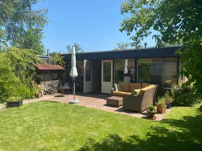 a patio with a couch and an umbrella in a yard at Casa Calida in Warmenhuizen