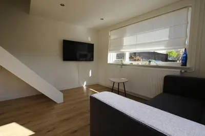 a living room with a couch and a television and a window at Have a nice stay! - Zomerhuis Benita's met parkeer plaats in Noordwijk aan Zee