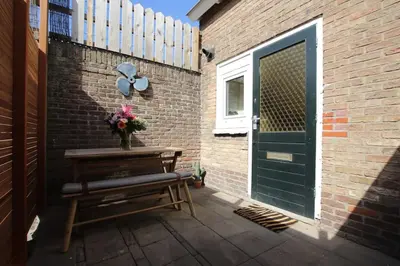 a patio with a bench and a green door at Have a nice stay! - Zomerhuis Benita's met parkeer plaats in Noordwijk aan Zee