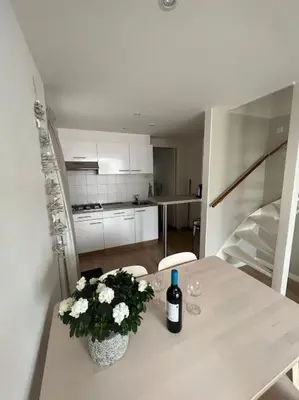 a white table with a bottle of wine and flowers on it at Have a nice stay! - Zomerhuis Toda Cambia dicht bij strand in Noordwijk aan Zee