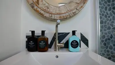 a bathroom sink with three bottles of soap and a mirror at Maun Apartment in Zandvoort