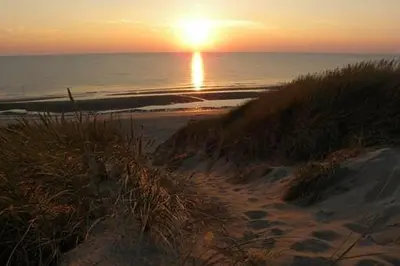 a sunset over a beach with the ocean and the sun at Gelijkvloers Vakantieappartement 150m van Strand Egmond aan Zee in Egmond aan Zee