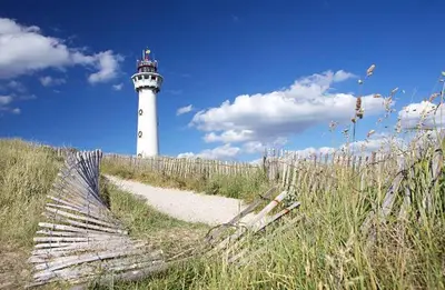 a lighthouse sitting on top of a beach with a fence at Studio aan Zee op 150 Meter van Strand in Egmond aan Zee