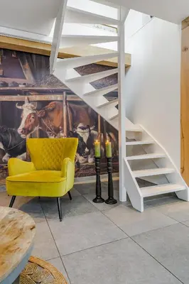 a living room with a yellow chair and a staircase at Luxury apartment in farmhouse near Amsterdam in Ilpendam