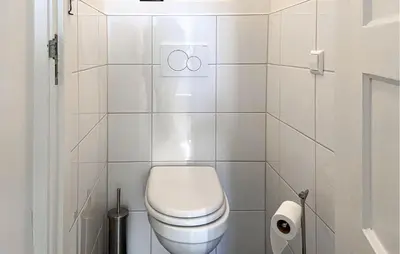a white bathroom with a toilet and a toilet paper dispenser at Klein Maar Fijn in Bergen