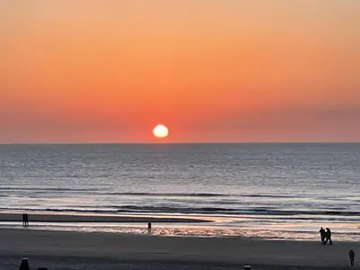 a sunset over the ocean with people walking on the beach at SATORI LODGE near the Dunes & the Beach in Zandvoort