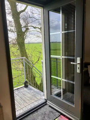 a door to a balcony with a view of a tree at De hoftuin Ilpendam appartement in Ilpendam