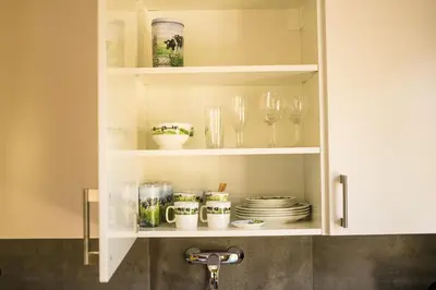 a kitchen cabinet with dishes and glasses and a sink at Bed & Breakfast Danina in Sassenheim