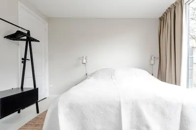 a white bedroom with a white bed and a window at The Garden Suite in Zandvoort