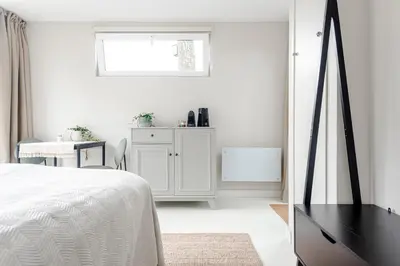 a white bedroom with a bed and a desk at The Garden Suite in Zandvoort