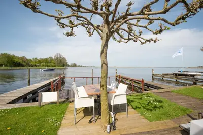 a table and chairs next to a tree on a dock at Meerzicht 99 - Luxury house 30 minutes from Amsterdam in Uitgeest