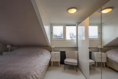 a bedroom with a bed and a chair and two windows at Meerzicht 99 - Luxury house 30 minutes from Amsterdam in Uitgeest