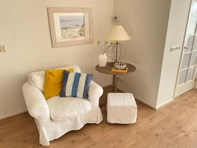 a living room with a white chair and a table at Amstel BeachHouse Egmond aan Zee, 50m from the beach! in Egmond aan Zee