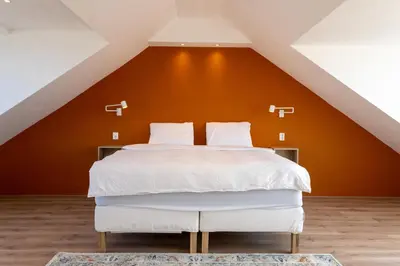 a bedroom with a white bed with an orange wall at Appartement aan Zee in Noordwijk aan Zee
